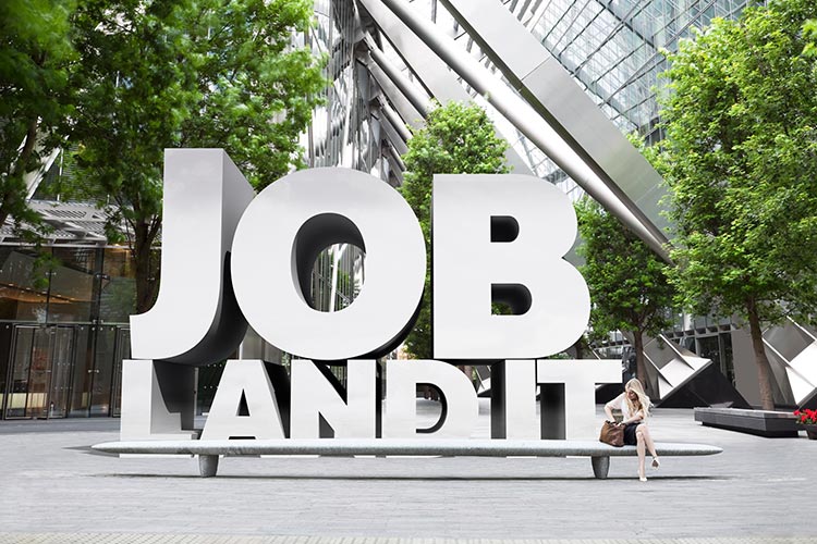 Campaign image for University of York careers and placements. Professional looking young woman in a modern office building, with huge 3D words "Job. Land It'" behind her. 