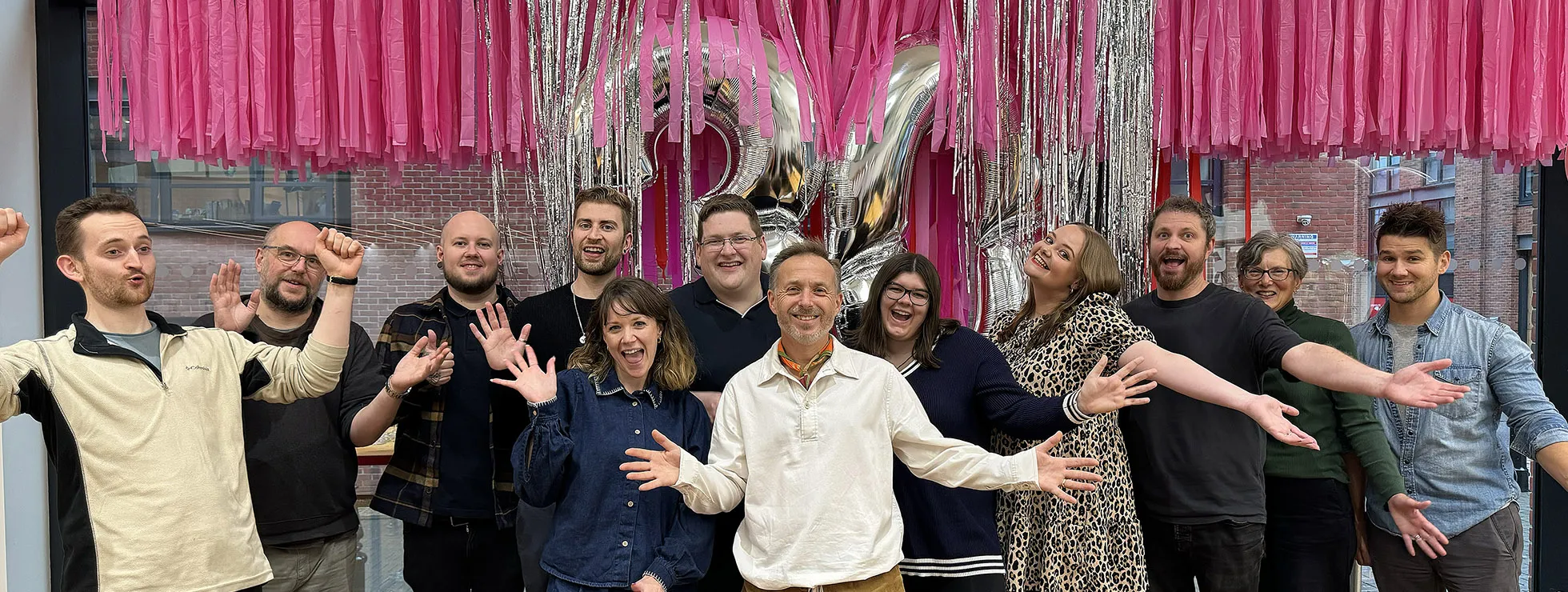 The IE team in the studio celebrating 30 years. Behind them  are pink and silver streamers and silver balloons in the shape of the number 30 